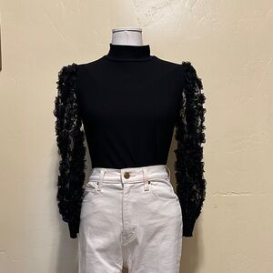 Black mock-neck top with embellished sleeves.